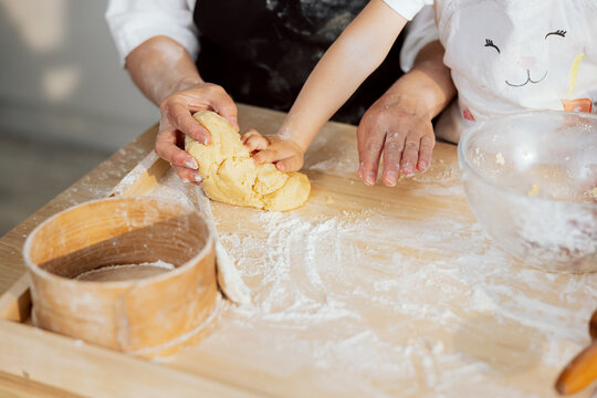 Close-up shot children small hands and eldrely woman kneading dough for baking cooking homemade pasta pizza bread muffin cookies pie on wooden surface in modern light kitchen.
