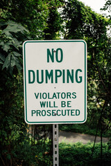 green and white metal "No Dumping" warning sign, violators will be prosecuted