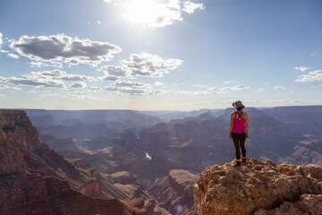 Adventurous Traveler standing on Desert Rocky Mountain American Landscape. Cloudy Sunny Sky. Grand Canyon National Park, Arizona, United States. Adventure Travel