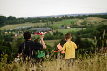 dad with two children are throwing airplanes in nature on a hill with a beautiful view