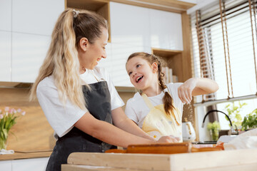Young beautiful daughter sprinkling dough with flour talking smiling. Mother teaching kneading...