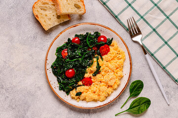 Cooked omelette and spinach with tomatoes on a light background