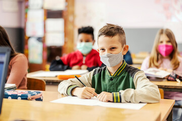 A schoolboy sits in class and writes schoolwork during corona virus.