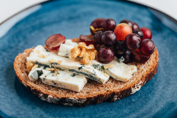 Open sandwich from toasted bread with mild creamy blue cheese, grapes and walnuts on blue plate