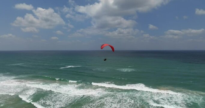 Powered paraglide flying above a Mediterranean beach.