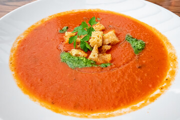 A traditional dish of Spanish and Italian cuisine is tomato soup with croutons and pesto sauce on a plate.