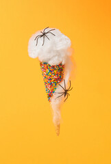 Minimal creative concept made of ice cream cone with sprinkles, spider's web and spiders on orange background. Scary and spooky Halloween concept. Abstract idea.