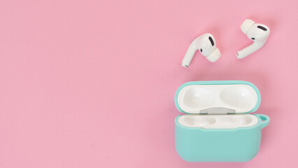 Wireless headphones in mint case on pink background, delicate background shades with space for text