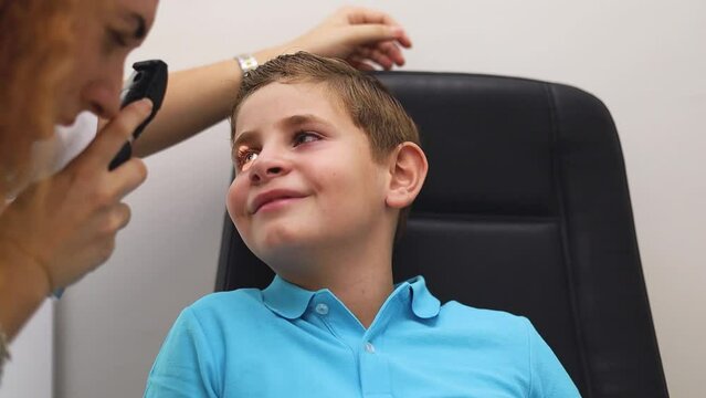 A female optometrist uses an ophthalmoscope to view the back of a child's eye.