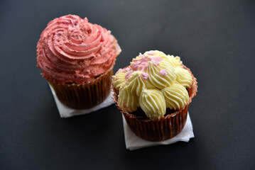 Sweet cakes with cream and sprinkles on a black background. Delicious pies for breakfast on black.