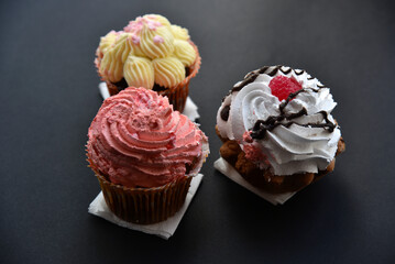 Sweet cakes with cream and sprinkles on a black background. Delicious pies for breakfast on black.