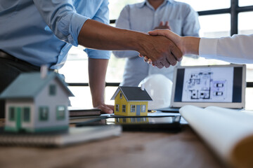 Close up of handshaking of engineer and architect after on paperworks and floor plan drawings about...