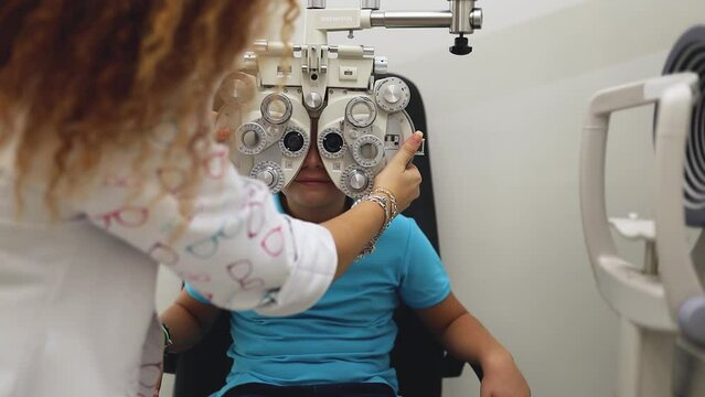 A female optometrist adjusts a phoropter to test a child's vision.