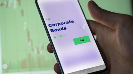 An investor's analyzing the corporate bonds etf fund on screen. A phone shows the ETF's prices corporate bonds to invest