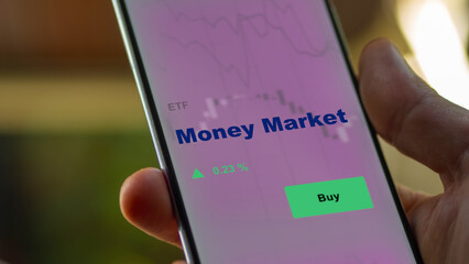 An investor's analyzing the money market etf fund on screen. A phone shows the ETF's prices to invest