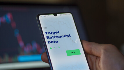 An investor's analyzing the target retirement date etf fund on screen. A phone shows the ETF's...