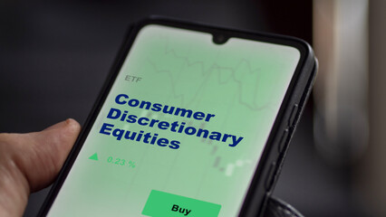 An investor's analyzing the consumer discretionary equities etf fund on screen. A phone shows the...