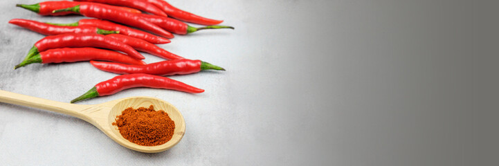 Ground red hot peppers in a wooden spoon and hot chili pods in the background. Spice for cooking spicy dishes. Banner with free space for text