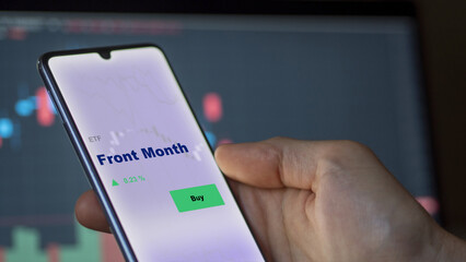 An investor's analyzing the front month etf fund on screen. A phone shows the ETF's prices web to invest