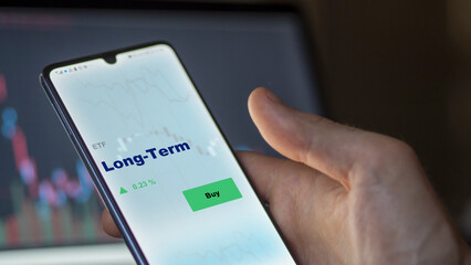 An investor's analyzing the long-term etf fund on screen. A phone shows the long term ETF's prices to invest.