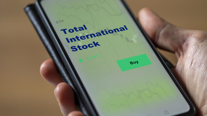 An investor's analyzing the total international stock etf fund on screen. A phone shows the ETF's prices stocks to invest