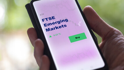 An investor's analyzing the FTSE emerging market etf fund on screen. A phone shows the ETF's prices stocks to invest