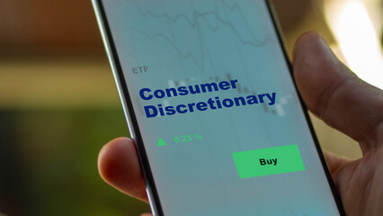An investor's analyzing the consumer discretionary etf fund on screen. A phone shows the ETF's prices stocks to invest - obrazy, fototapety, plakaty