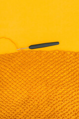 Top view of unfinished yellow crochet net with a hook inserted into a loop on bright yellow background