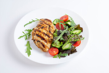 Tasty grilled chicken fillets on white plate with cherry tomatoes, arugula, lettuce and cucumber. Isolated on white background, top view