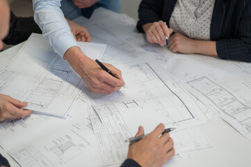 Close-up of the hands of four colleagues with blueprints on the table in the office. Brainstorming of engineers and architects.