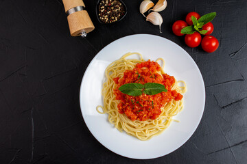 Top view of plate with spaghetti in tomato sauce and basil on dark background