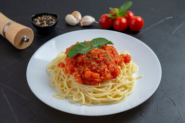 Top view of plate with spaghetti in tomato sauce and basil on dark background