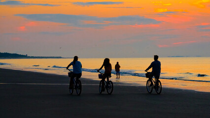 Sunrise at beach with silhouetted family on bicycles.