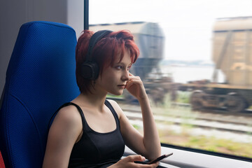 young woman rides on a commuter train and looks out the window at an outside landscape blurred in...