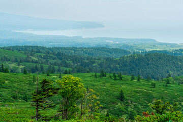 Naklejka premium typical landscape of the southern Kuriles, view of Kunashir Island from the slope of Golovnin volcano, slope of Mendeleyev volcano is visible in the distance in the haze