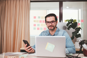 Portrait of smiling businessman with laptop sitting at desk in office. Cheerful casual caucasian employee, Handsome businessman using mobile phone. successful business working at office. mobile phone.