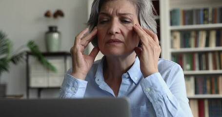 Tired overworked hoary mature lady touching face, rubbing temples, having headache, bad eye sight. Annoyed angry mature lady speaking about computer, software, online app work problems
