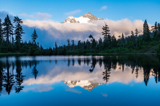 Mt Shuksan partially covered by cloud and its reflection in Picture Lake  under a blue sky in summer