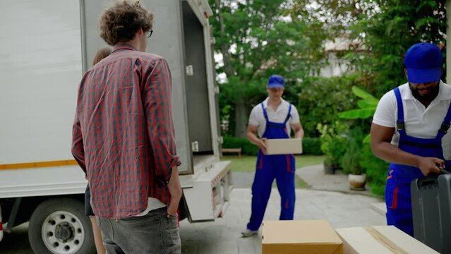 Moving service workers outdoors, unloading boxes and checking list is coming to deliver items to the family moving house.
