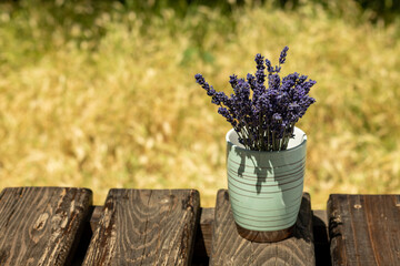 Bouquet of purple lavender flowers, in a green vase on a wooden background. Place for an inscription. Selective focus.