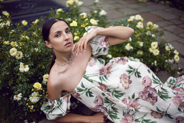 Outdoor portrait of a beautiful girl in a dress lying on the ground next to a white roses.