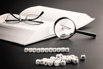 Word linguistics next to an open book, magnifying glass, pen and glasses. Concept of studying the...