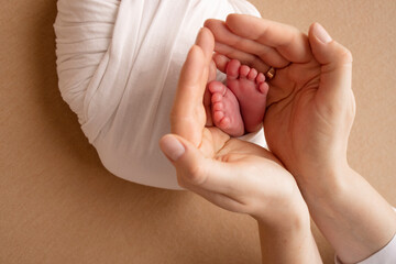 The palms of the parents. A mother hold the feet of a newborn child in a white blanket on a beige...