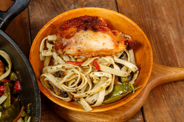 Udon with vegetables on the table in a wooden plate with sesame seeds near the frying pan fragment.