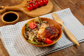 Udon with vegetables and chicken on the table in a wooden plate next to champignons and tomatoes on...