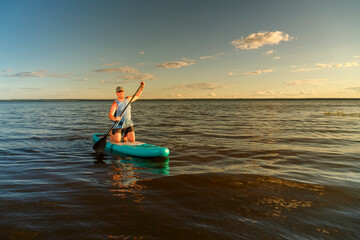Fototapeta na wymiar a man in shorts stands with a paddle on a SUP board at sunset in the lake.