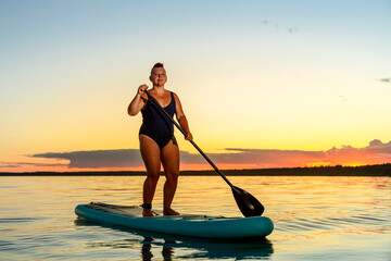 Jewish feminist woman in swimsuit shaved with mohawk on sup board at sunset.