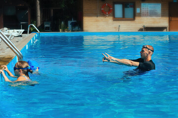 Swimming coach conducts a lesson with two girls in an outdoor pool with blue water on a warm sunny day