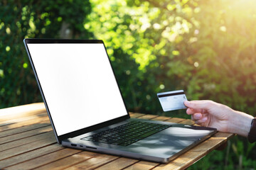 Young man using his credit card to pay online on his computer close-up view. Digital nomad working outside with white computer screen mockup