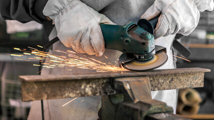 Craftsman grinding metal with disk grinder in workshop. Worker cleaning a steel
